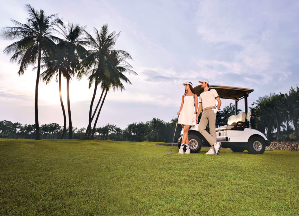 A couple in golf whites beside a golf cart on a course at sunset